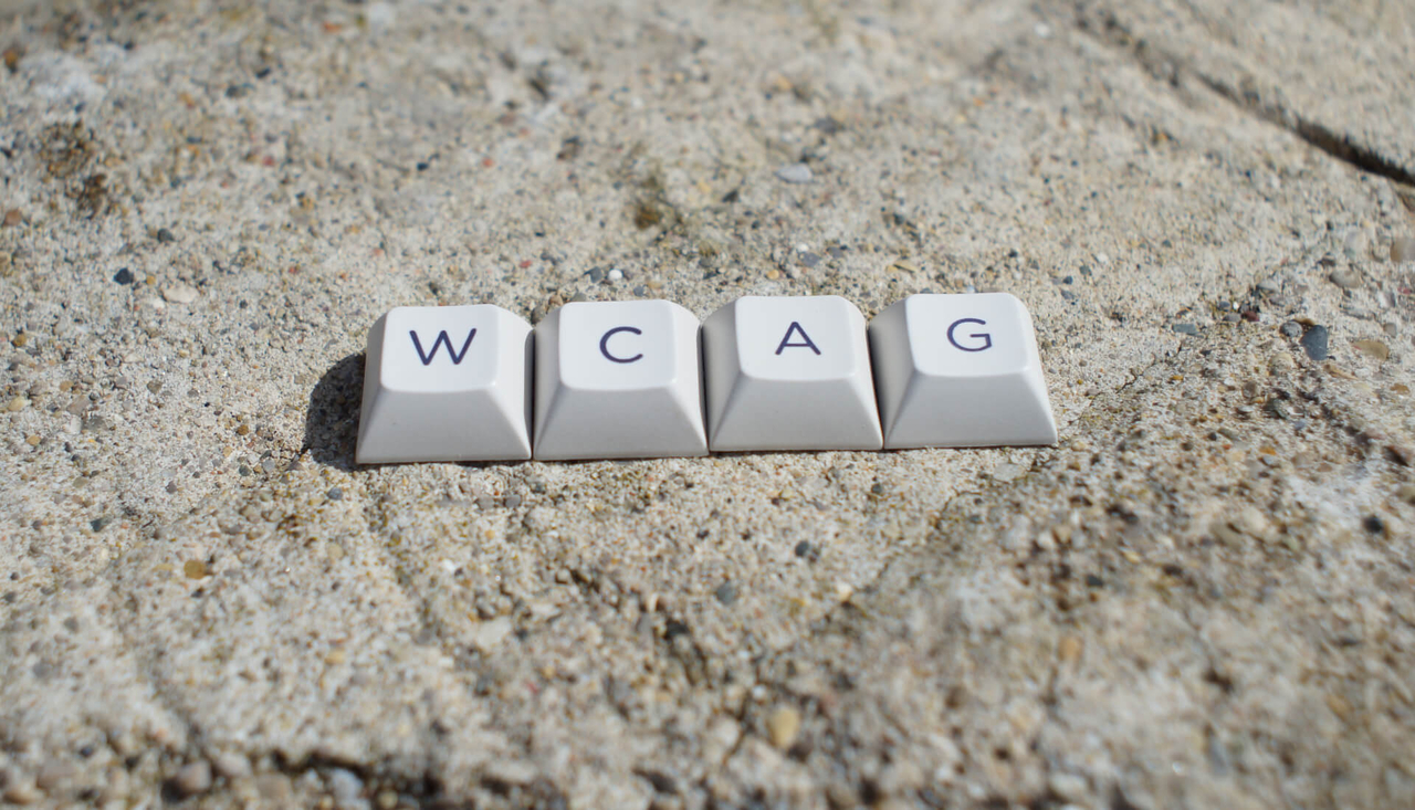 Four keyboard keycaps that spell out "WCAG" are placed on a large, grey rock.